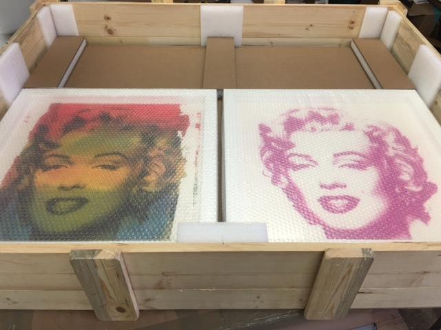 Two bubble-wrapped artworks of a woman in a wooden crate, ready for shipping.