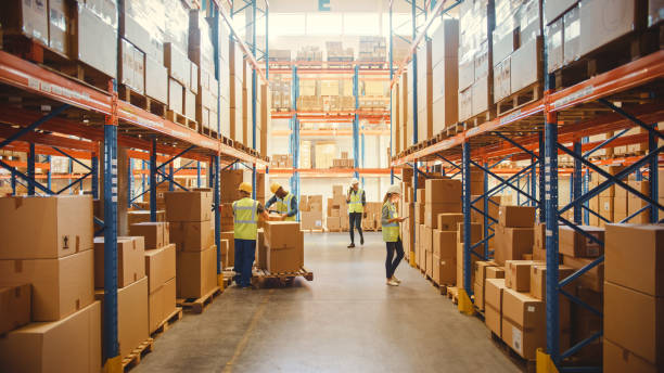 Workers packing and shipping boxes in a large warehouse with shelves filled with goods.
