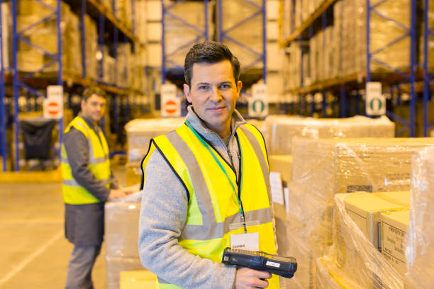 Two warehouse workers in safety vests manage packages in a shipping facility.