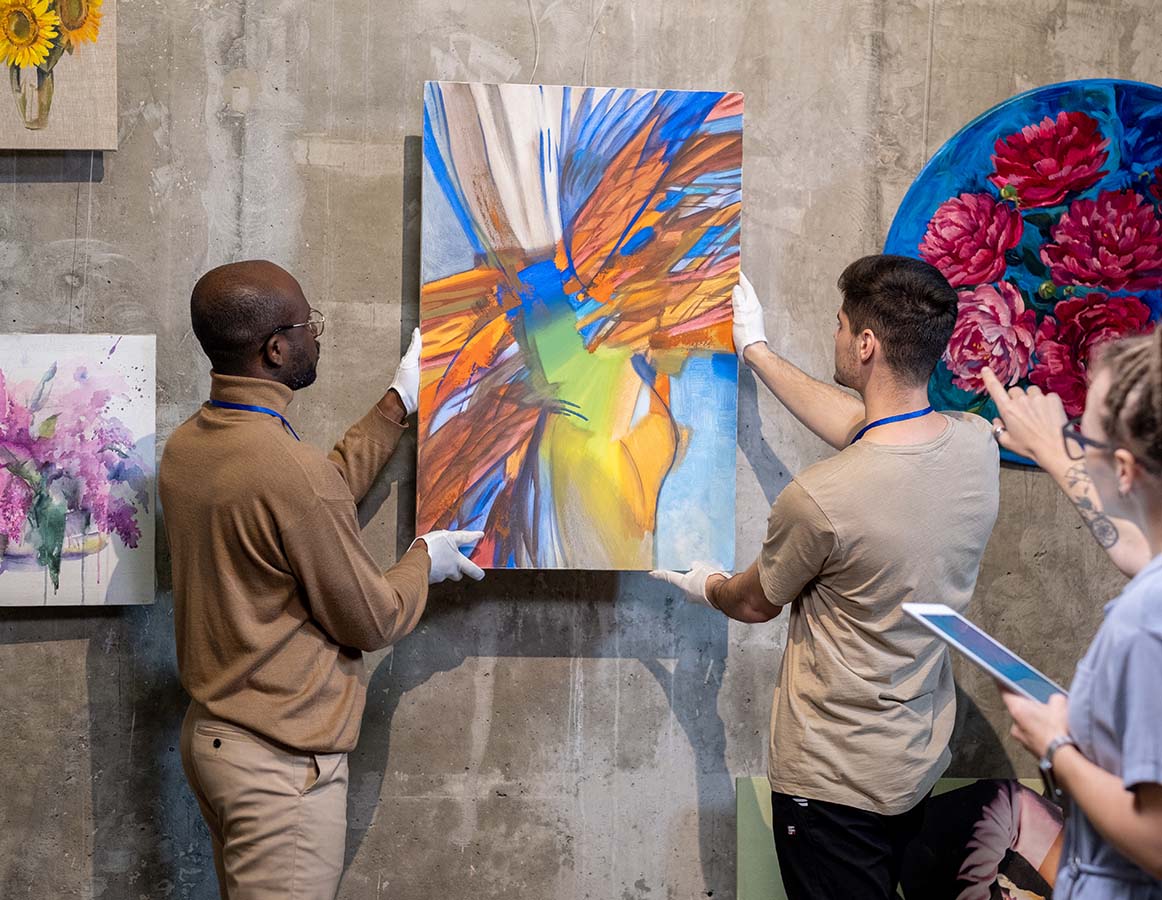 Goodman Packing and Shipping team members  work on alignment of painting as part of an exhibit.